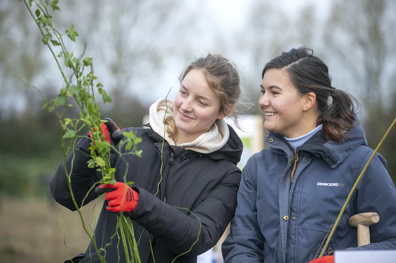 Twee meisjes kijken naar een jonge boom die in Nederland geplant zal worden