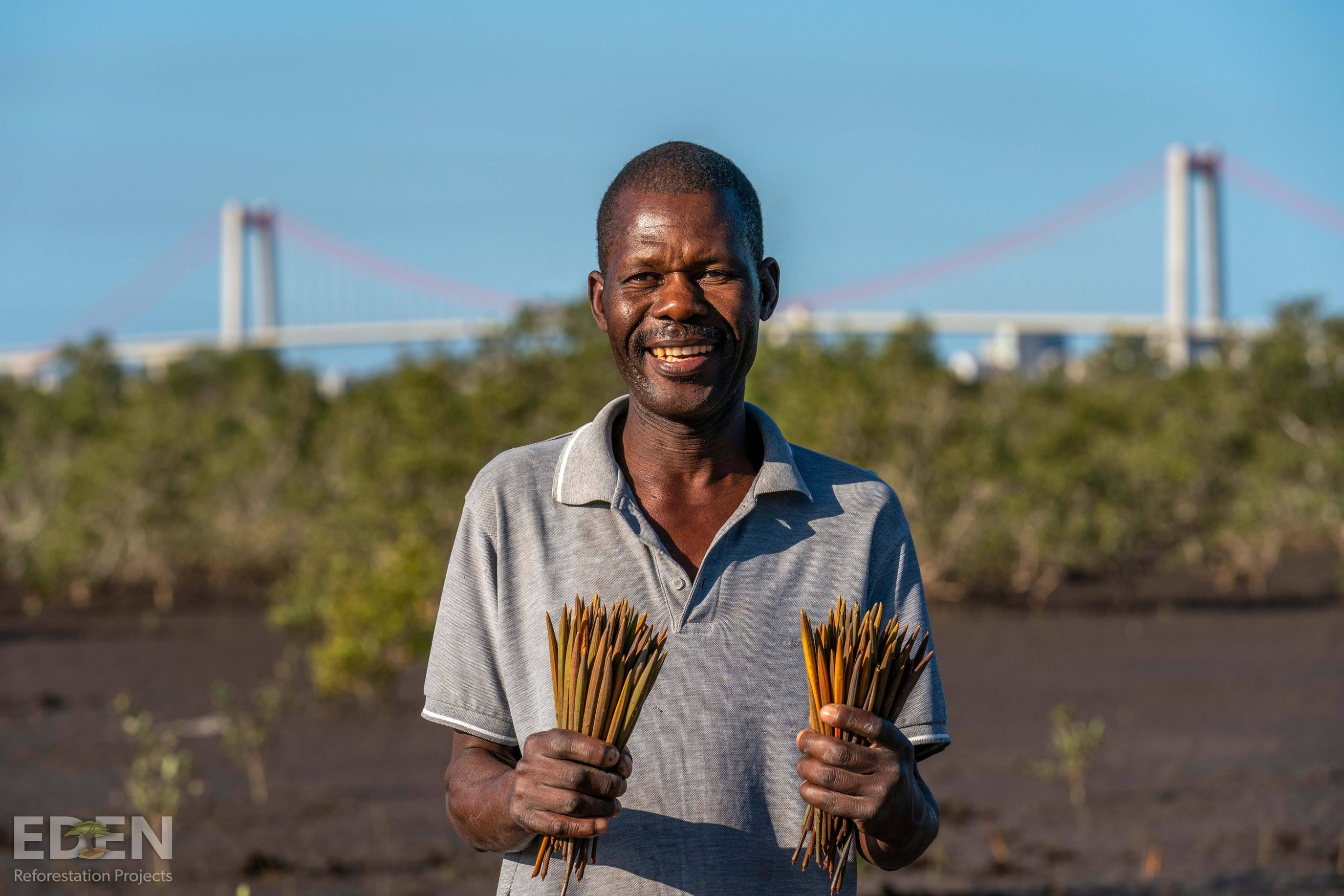 Plaatselijke bewoner lacht naar de camera tijdens het planten van mangrove zaailingen